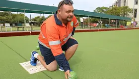a man kneeling on a green surface with a ball