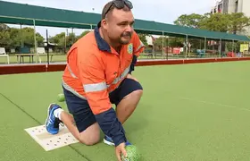 a man kneeling on a green surface with a ball