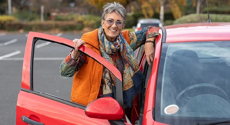 Person standing beside an open red car door in a car park.