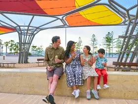 A family sitting under Weaving of Stories by Sharyn Egan