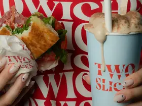 Someone holding a Two Slices sandwich and a latte