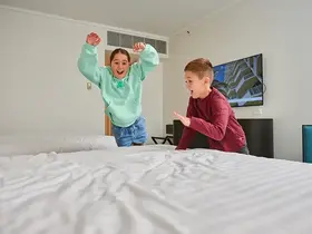 Two children jumping on to a hotel room bed