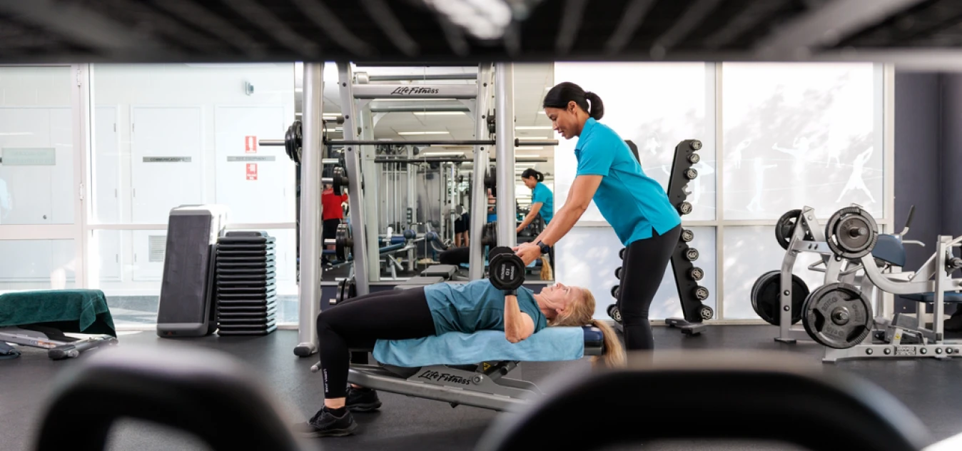 REC_InglewoodGym_1348x632 A staff member spotting a woman lifting weights