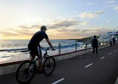 a man riding a bike on a road next to a body of water