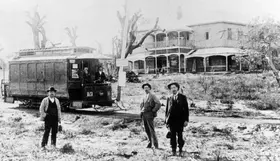 A black-and-white image of three men near a tram