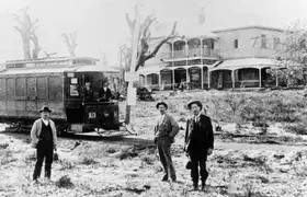 A black-and-white image of three men near a tram