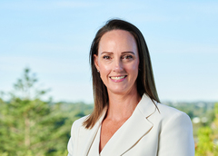 Head-and-shoulders portrait of a person with straight, shoulder-length dark hair wearing a light beige blazer over a light top. 