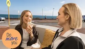Two women holding coffees by the beach
